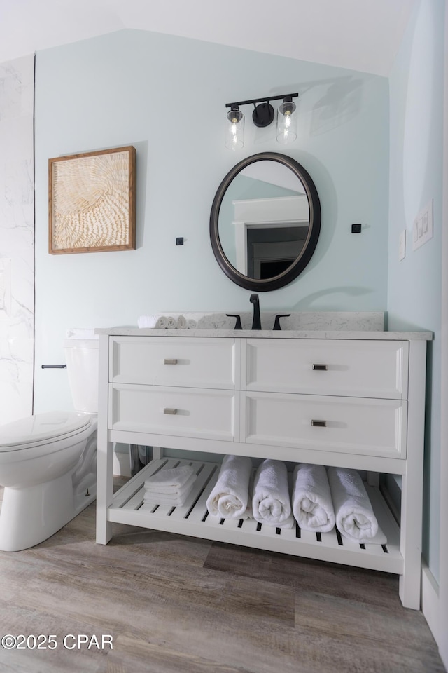 bathroom featuring lofted ceiling, toilet, vanity, and wood finished floors