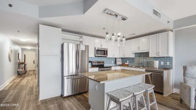 kitchen with appliances with stainless steel finishes, a kitchen island, decorative light fixtures, white cabinetry, and sink