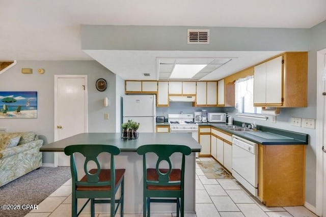 kitchen with a center island, dark countertops, visible vents, white appliances, and under cabinet range hood