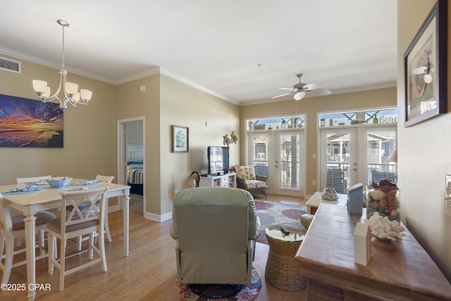 living room with light wood-type flooring, crown molding, ceiling fan with notable chandelier, and french doors