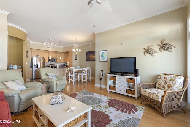 living room with ceiling fan with notable chandelier, crown molding, track lighting, and light hardwood / wood-style flooring