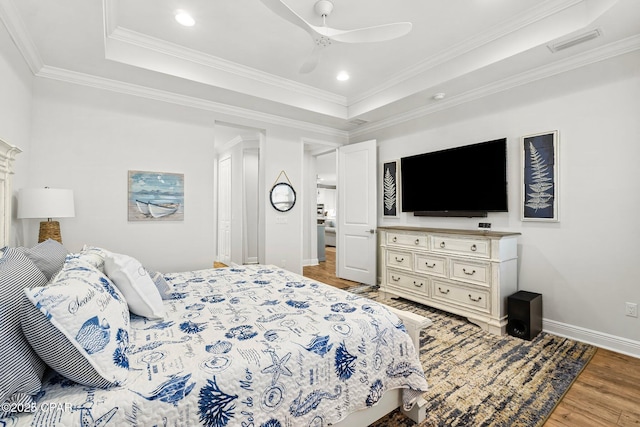 bedroom with ceiling fan, ornamental molding, a tray ceiling, and light hardwood / wood-style floors