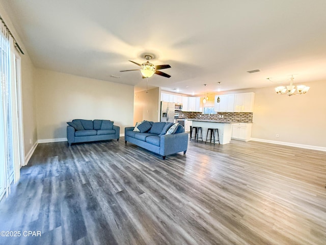 living room featuring ceiling fan with notable chandelier, baseboards, and wood finished floors