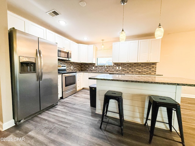 kitchen featuring tasteful backsplash, visible vents, a breakfast bar area, wood finished floors, and stainless steel appliances