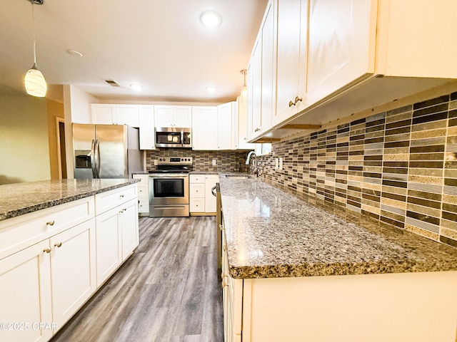 kitchen with wood finished floors, a sink, visible vents, appliances with stainless steel finishes, and backsplash