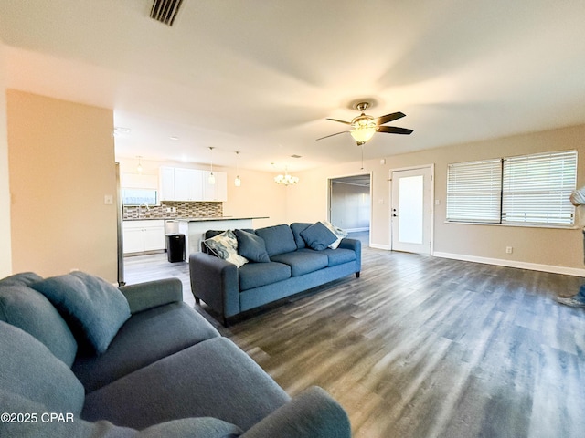 living room featuring ceiling fan with notable chandelier, dark wood-style flooring, visible vents, and baseboards