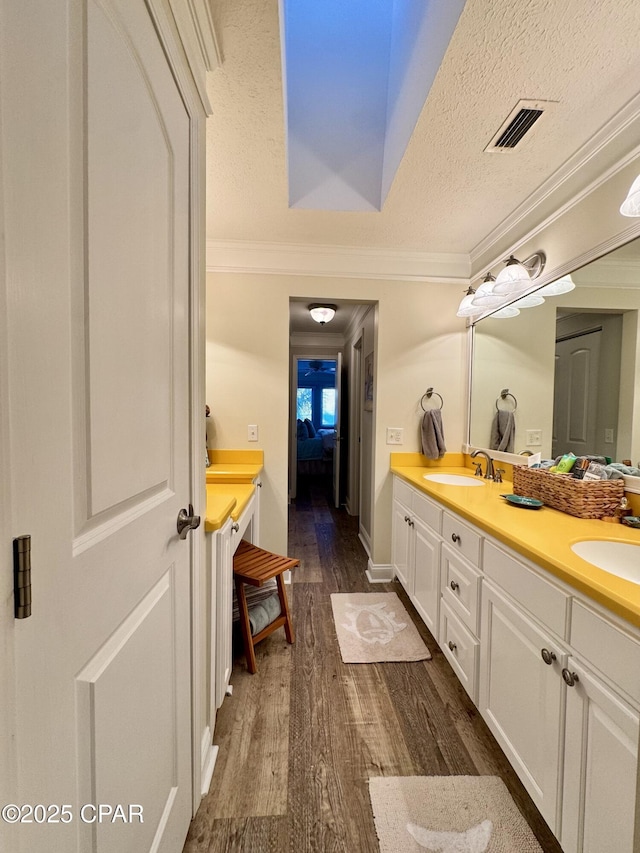 bathroom with ornamental molding, wood-type flooring, vanity, and a textured ceiling