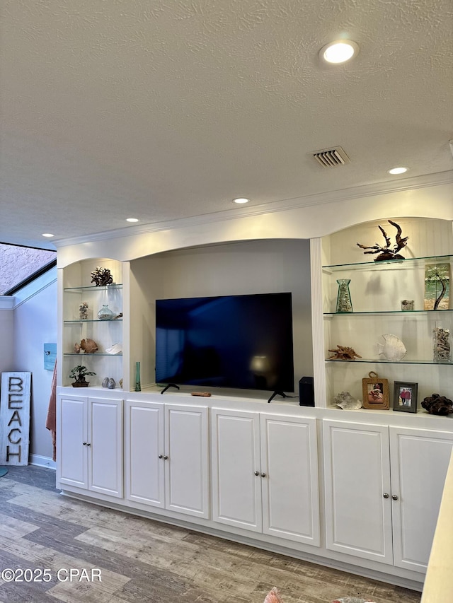 living room featuring built in shelves, ornamental molding, light hardwood / wood-style floors, and a textured ceiling