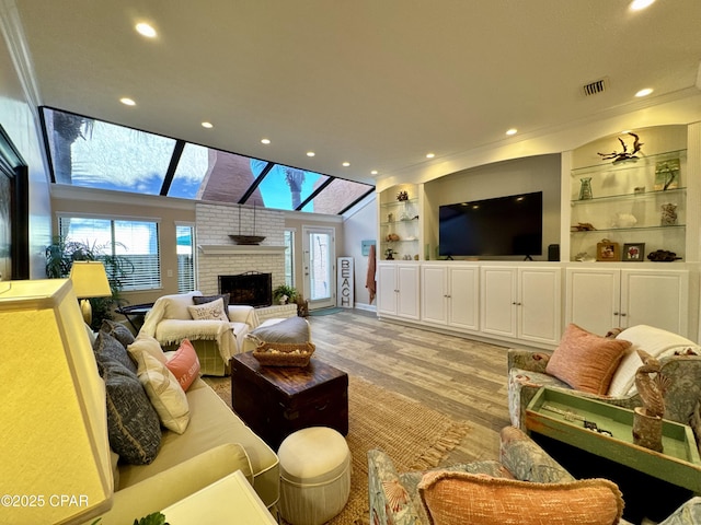 living room with ornamental molding, a brick fireplace, light hardwood / wood-style flooring, and built in shelves