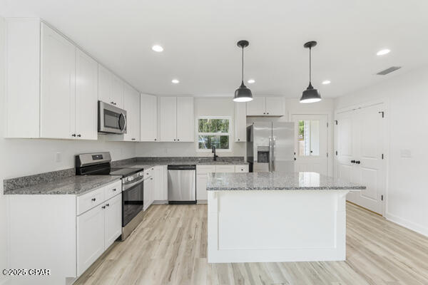 kitchen with stainless steel appliances, white cabinetry, hanging light fixtures, and a center island