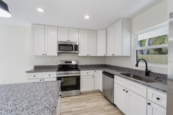 kitchen with sink, appliances with stainless steel finishes, light hardwood / wood-style floors, white cabinets, and dark stone counters