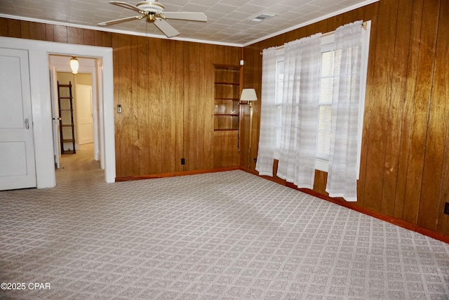 carpeted empty room featuring ornamental molding, ceiling fan, and wood walls