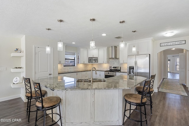 kitchen with pendant lighting, white cabinets, wall chimney exhaust hood, stainless steel appliances, and sink