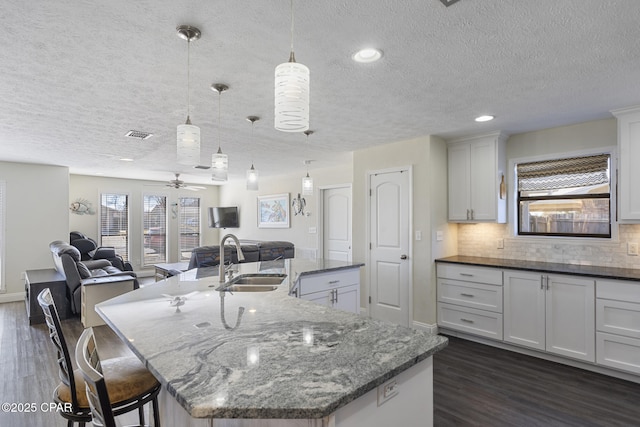 kitchen with ceiling fan, a large island with sink, sink, white cabinetry, and hanging light fixtures