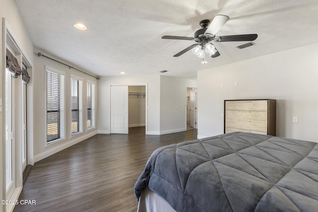 bedroom with ceiling fan, dark wood-type flooring, a textured ceiling, a walk in closet, and a closet