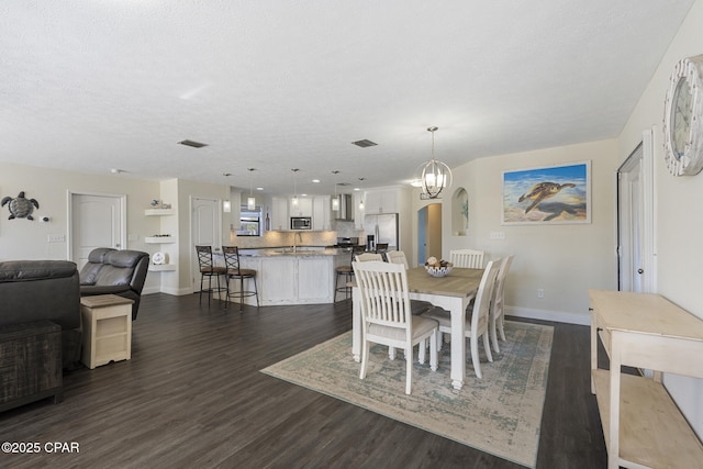 dining area featuring a textured ceiling, dark wood-type flooring, sink, and a notable chandelier