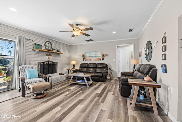 living room with a brick fireplace, hardwood / wood-style floors, crown molding, and ceiling fan