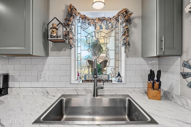 kitchen featuring backsplash, light stone counters, sink, and gray cabinetry