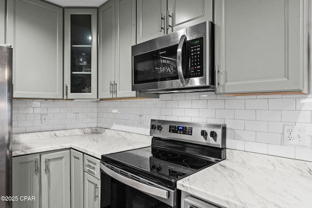 kitchen featuring light stone countertops, appliances with stainless steel finishes, decorative backsplash, and gray cabinets