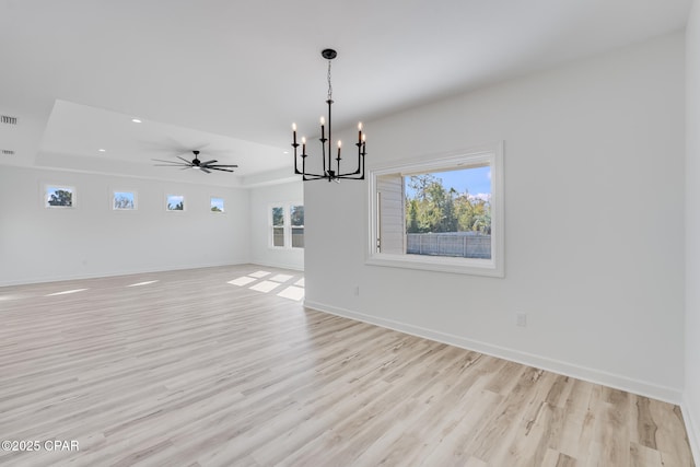 interior space with light wood-type flooring, ceiling fan with notable chandelier, and a tray ceiling