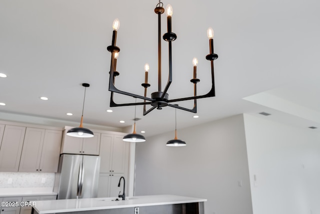 room details with a kitchen island with sink, decorative backsplash, hanging light fixtures, and stainless steel refrigerator