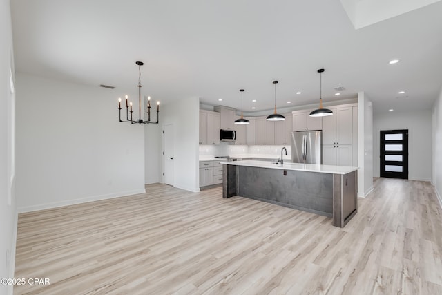 kitchen with pendant lighting, light hardwood / wood-style flooring, a kitchen island with sink, a chandelier, and stainless steel appliances