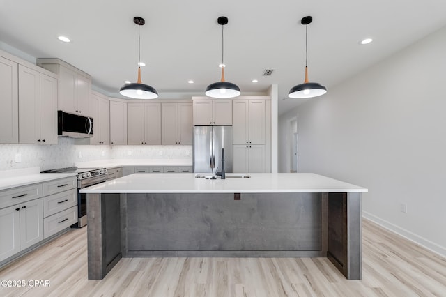 kitchen with sink, a kitchen island with sink, hanging light fixtures, and stainless steel appliances