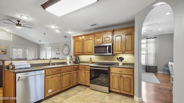 kitchen featuring a textured ceiling, appliances with stainless steel finishes, lofted ceiling, sink, and kitchen peninsula