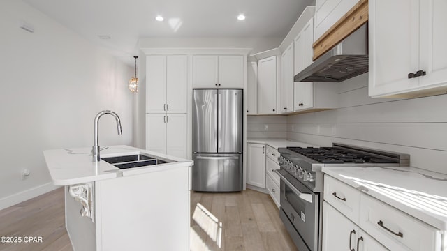 kitchen with pendant lighting, appliances with stainless steel finishes, light hardwood / wood-style floors, sink, and a center island with sink