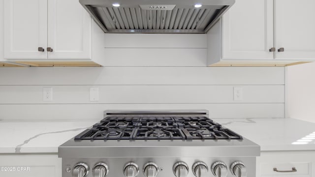 kitchen with premium range hood, stainless steel stove, white cabinets, and light stone countertops