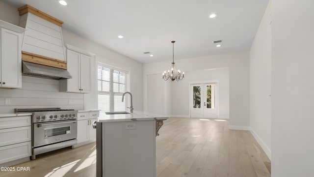 kitchen with high end range, sink, a notable chandelier, a center island with sink, and range hood