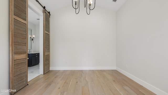 unfurnished room featuring light wood-type flooring, vaulted ceiling, and a barn door