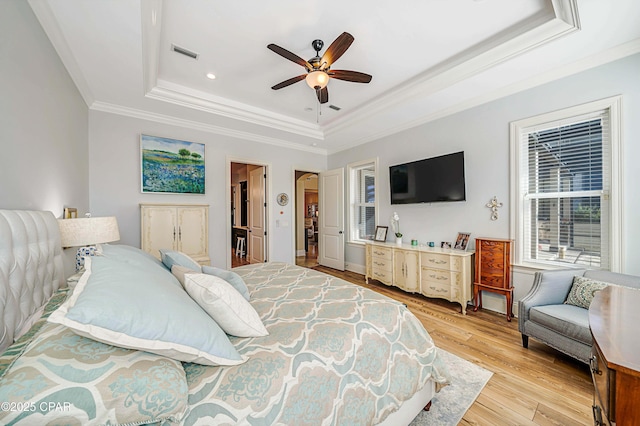 bedroom with a tray ceiling, crown molding, light wood finished floors, visible vents, and ceiling fan