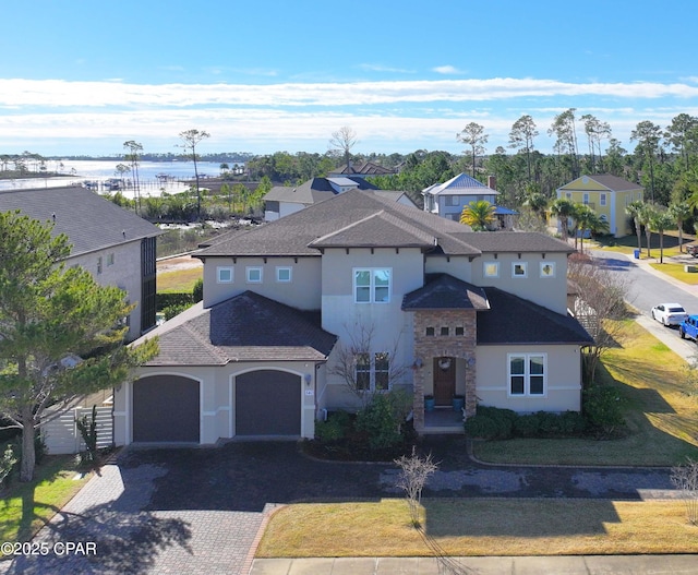 view of front of house featuring decorative driveway, stucco siding, a shingled roof, a garage, and stone siding