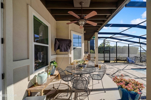 view of patio with outdoor dining area, glass enclosure, and ceiling fan