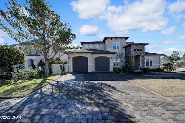 view of front of house featuring stone siding, an attached garage, fence, decorative driveway, and stucco siding