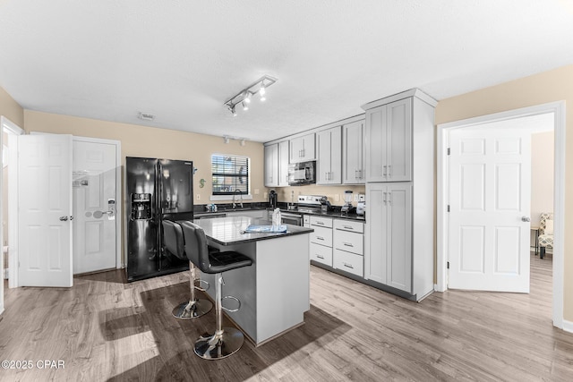 kitchen featuring a kitchen bar, gray cabinets, light wood-type flooring, black appliances, and a center island