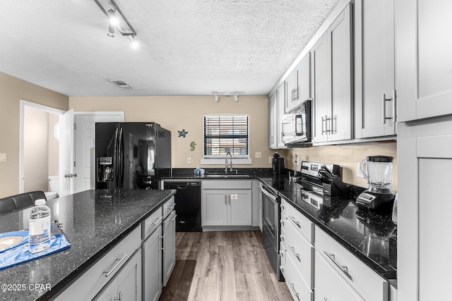 kitchen with dark stone countertops, a textured ceiling, black appliances, light hardwood / wood-style flooring, and sink