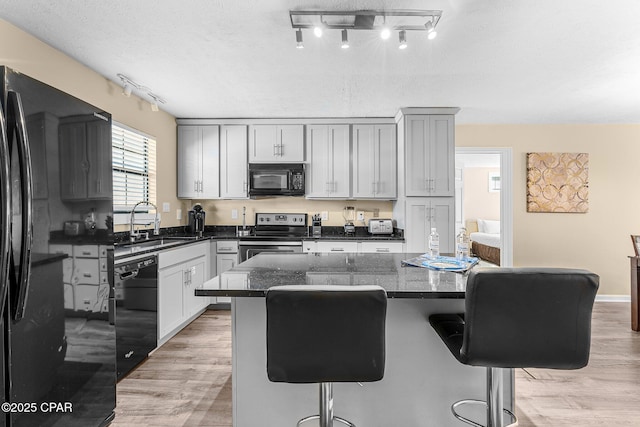 kitchen featuring black appliances, a kitchen island, a kitchen bar, dark stone countertops, and sink