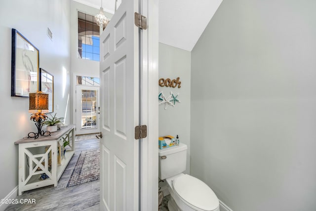 bathroom featuring wood-type flooring, an inviting chandelier, toilet, and a high ceiling