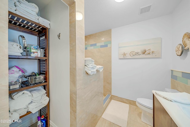 bathroom with tile patterned floors, vanity, a tile shower, and toilet