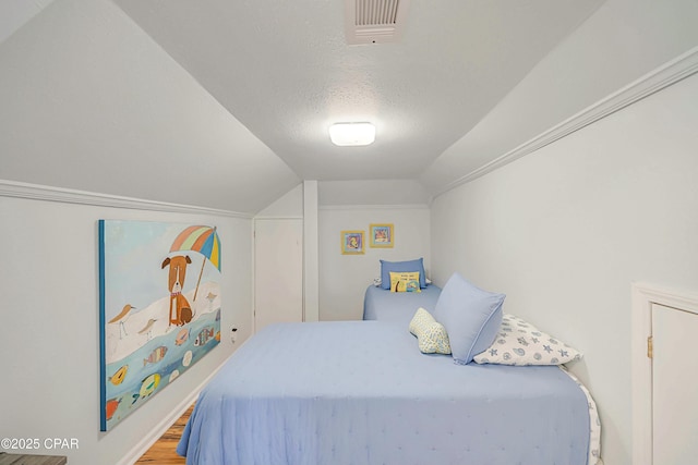 bedroom with vaulted ceiling, hardwood / wood-style floors, a textured ceiling, and crown molding