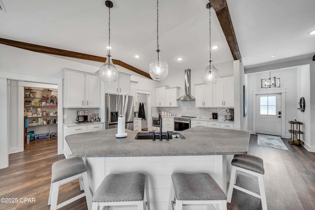 kitchen featuring beamed ceiling, sink, white cabinets, stainless steel appliances, and wall chimney exhaust hood