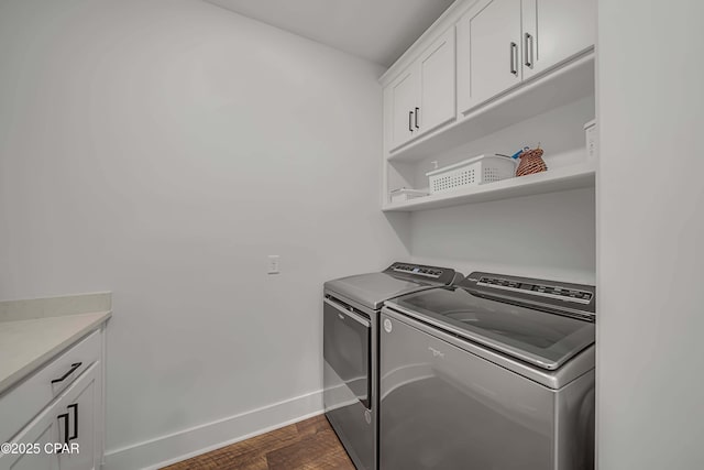 laundry area featuring dark wood-type flooring, washer and clothes dryer, and cabinets