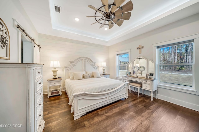 bedroom featuring dark hardwood / wood-style flooring, ceiling fan, a barn door, and a raised ceiling