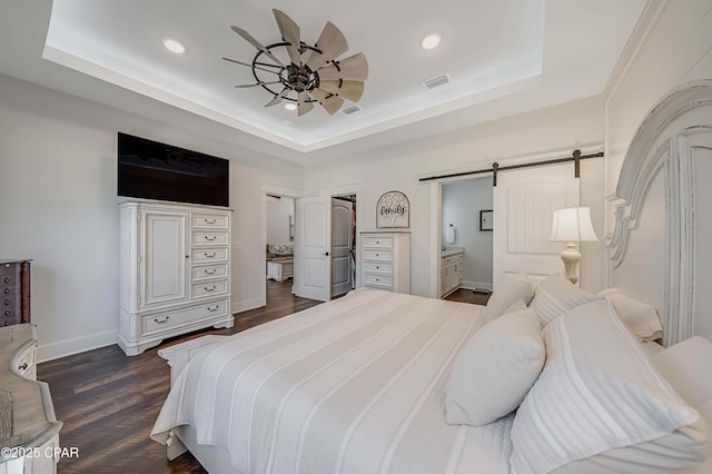 bedroom featuring ensuite bath, ceiling fan, a tray ceiling, dark hardwood / wood-style flooring, and a barn door