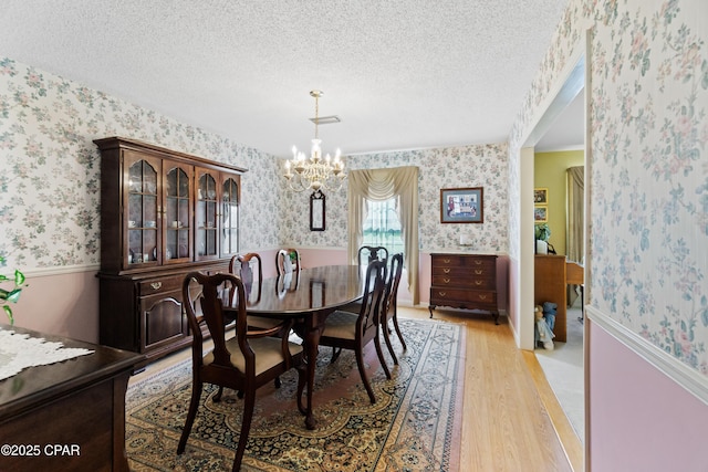 dining space featuring a chandelier, light hardwood / wood-style flooring, and a textured ceiling