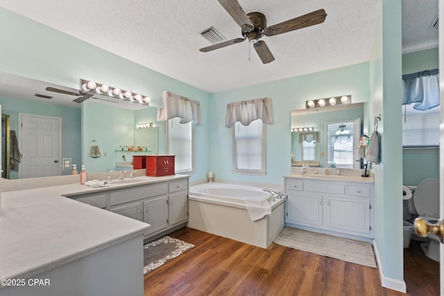 bathroom with a textured ceiling, hardwood / wood-style floors, vanity, a tub, and ceiling fan