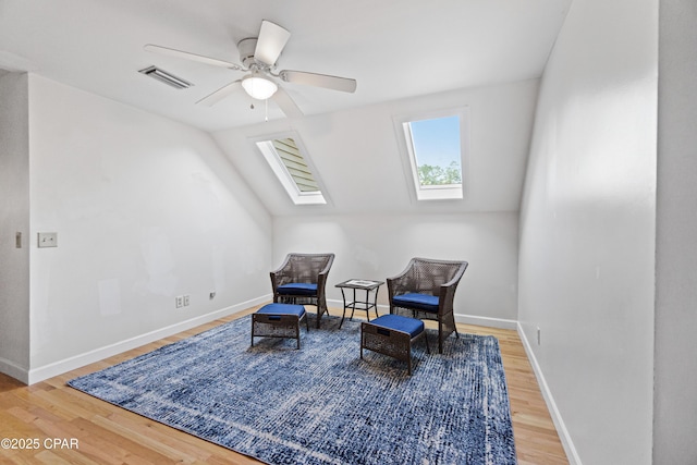 living area with ceiling fan, lofted ceiling with skylight, and hardwood / wood-style floors