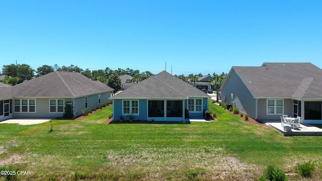 back of house featuring a patio, a lawn, and roof with shingles